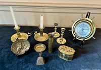 Photo of entire brass collection showing chambersticks, barometer, candlesticks, incense burner, and eagle dish on display surface.