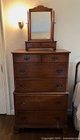 Full front view of maple chest-on-chest dresser with brass bail pulls and valet mirror on top.