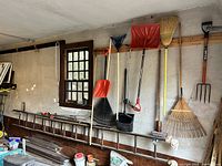 Full view of the vintage wooden extension ladder lying on the floor with assorted garden tools hanging on the wall above it.