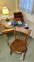 Wooden Leg-o-Matic card table with green vinyl top, stacked wooden card holders, assorted playing cards and Canasta booklets, wooden hobnailed desk lamp, and rod-back Windsor side chair.