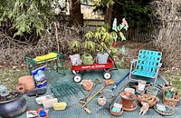 Wide view of garden items including planters, wagon, bench, chair, decor, and rug spread outdoors.