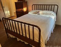 Full view of mahogany Jenny Lind double bed with spindle headboard and footboard, white vintage cotton matelasse coverlet with bobble trim covering mattress, floral pillow on top