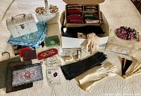 Wide view of lot showing woven rattan purses, assorted coin purses, fabric gloves, small wallets and pouches laid out on quilted surface.