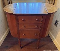 Front view of wooden Martha Washington style sewing cabinet closed showing side lids and three drawers.