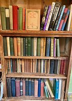 Four wooden shelves filled with mostly vintage hardcover books in assorted colors and sizes, including some with dust jackets.