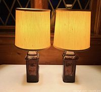 Pair of amethyst purple glass lamps with clip-on fabric drum shades on a white surface against wooden background.