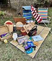 Wide view of the entire picnic and beach set showing baskets, mats, chairs, dishware, lanterns, and bags on a straw mat outdoors.