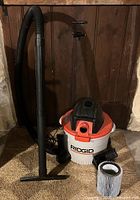 Full view of the Ridgid 9 gallon wet dry vacuum with extension hose, flat nozzle, and cylindrical pleated filter cartridge positioned on the floor.