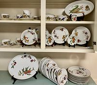 Image showing multiple plates on stands and stacked, including salad and dinner plates with autumnal fruit designs.