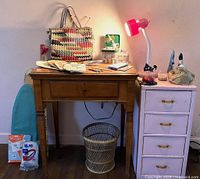 Singer sewing machine wooden cabinet with drawers and sewing accessories on and around it, including task lamp, scissors, pressing board, and baskets.