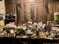 Work bench with multiple saws hanging on a wooden wall and a cluttered tabletop with tools, lightbulbs, and various hardware.