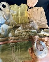 Overview of vintage baby and doll clothes including dresses, bonnets, bibs, and bed jackets in pastel colors and delicate fabrics
