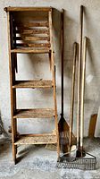 Front view of pine step ladder with three garden tools (two rakes and one spade)