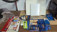 Overview of art supplies on a table including sketch pads, colored pencils, pastels, rulers, and brushes.