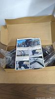 Open cardboard box containing black metal bike surfboard bracket parts and installation manual