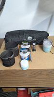 Camping cookware set with collapsible cup, cooking pots, lantern/light, all placed next to the tent bag.
