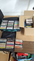 Photo showing multiple cassette tapes stored in a black zipper case and cardboard boxes on a wooden surface.
