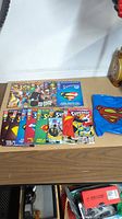 Photo showcasing a collection of Reign of Superman comics and a blue Superman cape with red logo on a table.