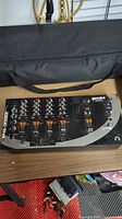 Top view of Gemini PS-700 mixer inside black carrying case on wooden table with visible knobs and faders.