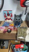 Photo showing the lot of various holiday-themed items arranged on a table, including a snowman tote, wolf mask, pumpkin decoration, candle holder, and packaged confetti.