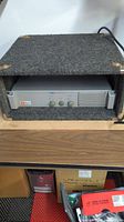 JBL SR6615 power amplifier housed inside a carpeted enclosure, showing overall front view, unit powers on.