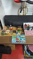 Overview of the table with vintage diecast cars spread out, showing various models and colors including trucks and regular cars along with a popcorn container holding more cars.