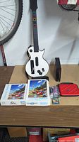 Overall lot showing guitar controller, puzzles, games, red case, and black box