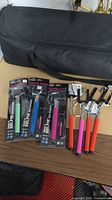Photo of 3 selfie sticks in original packaging and 4 loose selfie sticks with colored rubber handles on table