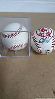 Two baseballs side-by-side on a table; one in a clear protective case signed by Jon Lester, the other with Boston Red Sox logo signed by Coco Crisp.