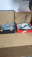 Two pairs of Nike sneakers in their boxes on a wooden surface.