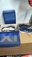 Two pairs of Nike sneakers on a table with one pair in original blue Air Jordan 11 box with large XI on lid