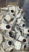 Clear photo showing multiple white Baby Delight security cameras with power cables and mounting brackets piled inside a large plastic tote.