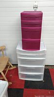 Photo of two plastic storage drawer units stacked; pink 4-drawer unit on top of white translucent 4-drawer unit, placed on black and red checkered floor next to a wooden chair.