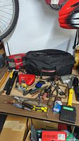 Wide view showing tool bag and assortment of hand tools and chargers on wooden table