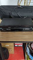 Toshiba DVD VCR combo unit placed on brown wooden surface with black carrying case in background.