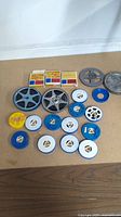 Vintage 8mm and Super 8 film reels with plastic cartridges laid out on table showing various colors and sizes.