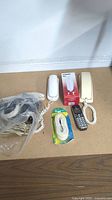 Photo showing two corded phone handsets, one cordless phone, Vtech handset box, and two phone cords on floor.