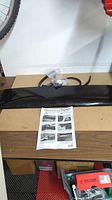 Photo of black WeatherTech sunroof wind deflector placed on table along with installation instruction sheet and mounting hardware bag.