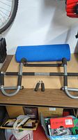 Metal chin up bar with foam handles and a rolled blue yoga mat on a table