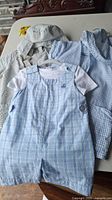 Photo showing the 3 boys summer outfits laid out, including light blue checkered romper with white undershirt and two hooded shirts in blue and green gingham pattern.