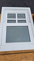Front view of a small white framed window showing a divided top section with four panes and a single large bottom pane.