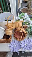 Photo of group of assorted wicker baskets, large fabric lamp shade, artificial white flowers, and lighted garland on table