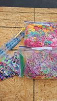 Photo showing a blue Rainbow Loom bracelet maker device and three large zip-lock bags filled with various colored rubber bands for crafting bracelets.