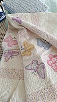 Close-up of quilt showing colorful butterfly appliqué on textured cream background.