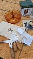 Photo showing the vintage amber glass divided candy dish, Pampered Chef cheese set with wooden handles and tools in a canvas pouch, and a boxed mug.