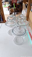 Five clear glass round jars with matching clear lids arranged on white table.