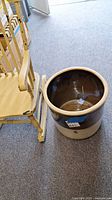 Wide view showing the crock next to a chair to indicate size and condition.