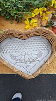 Wicker heart-shaped basket with perforated metal tin punch insert featuring two bird designs, set atop straw mat and surrounded by yellow floral wreath.
