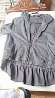 Dark grey medium size girls zip-up hoodie with ruffled hem detail and hood, laid flat on surface