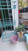 Metal wire storage rack with multiple baskets, ceramic planter, two artificial plants in beige pots, gray plastic basket with wooden handled brush.